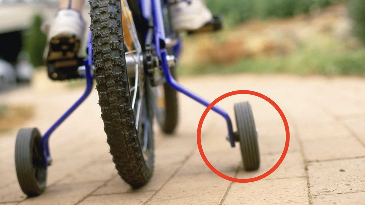 A bicycle with training wheels. One of the training wheels is highlighted with a red circle.
