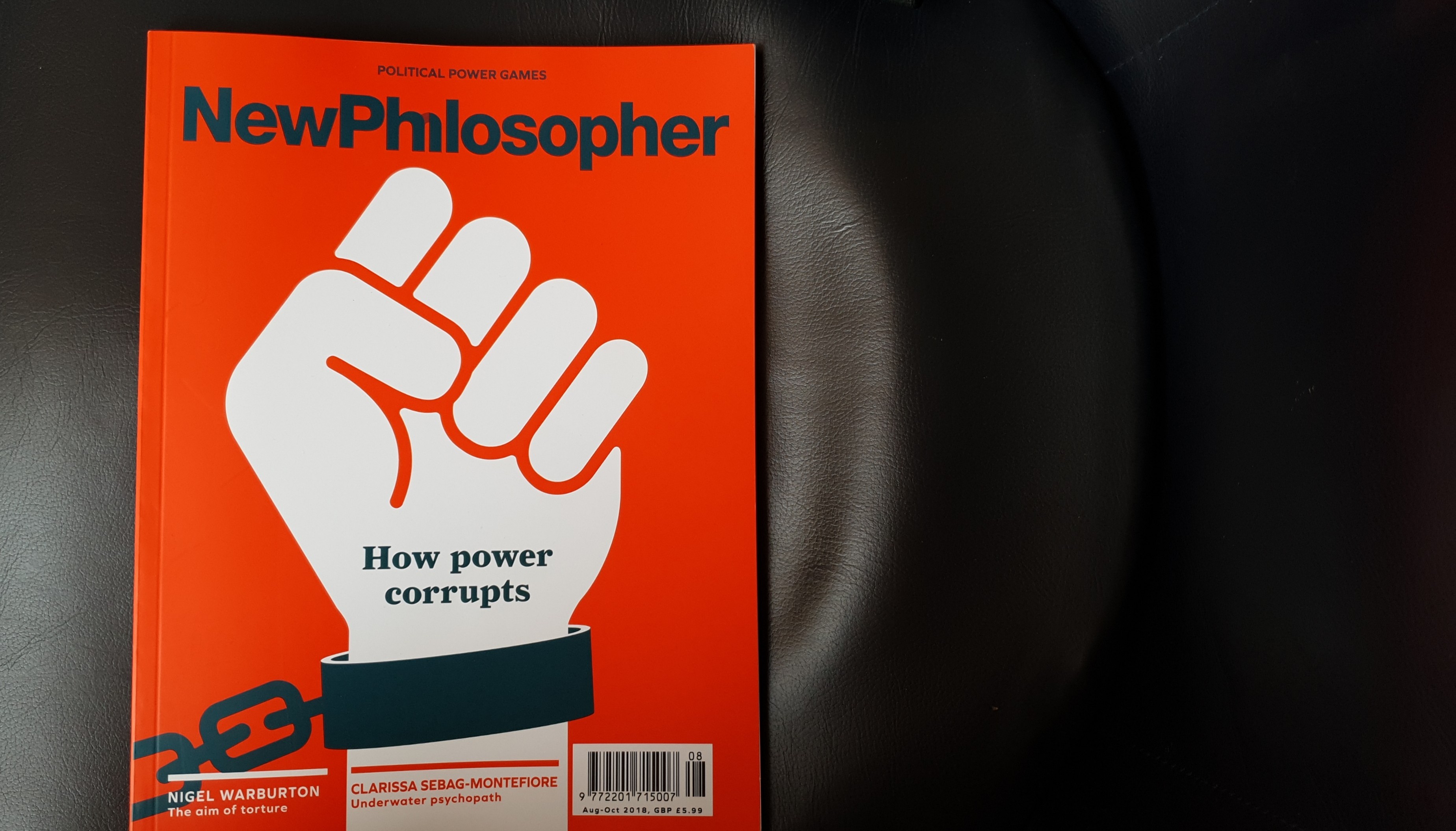 The cover of New Philosopher magazine. Red background with a flat illustration of a raised fist in white, shackled at the wrist with the chains of the shakle disappearing off page lower left. The headline is 'how power corrupts'