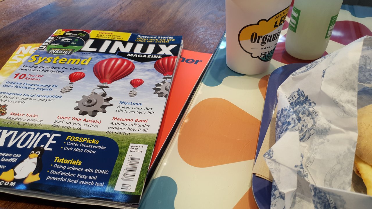 Table top with three magazines: Linux Magazine on top with bits of New Scientist and New Philosopher showing underneath. Partial: coffee cup, lemonade, and muffin.