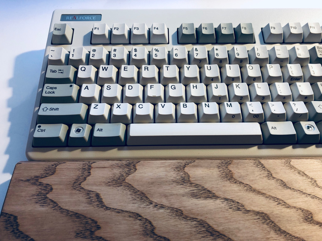 A Topre Realforce 87UW 55g ANSI US layout keyboard with white and grey keys and a Filco wooden wrist rest.