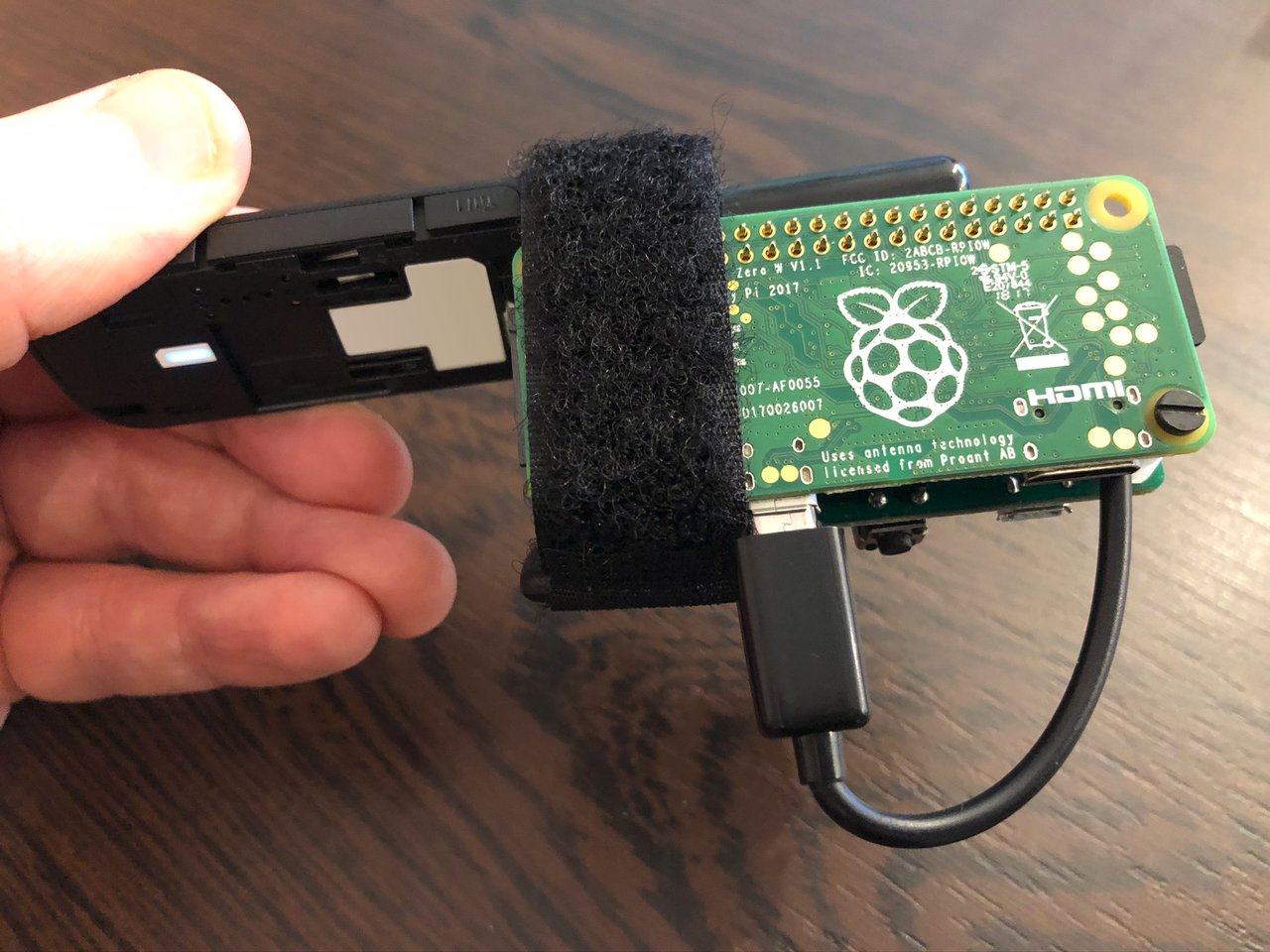 Photo of Prototype-01 bound with the velcro strap and in my hand showing the back of the Raspberry Pi with the raspberry logo.